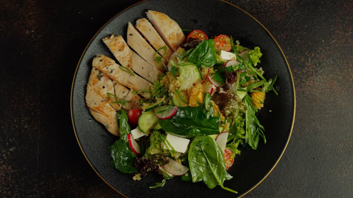 Top view of a delicious chicken salad with fresh vegetables on a black plate, perfect for a healthy meal.